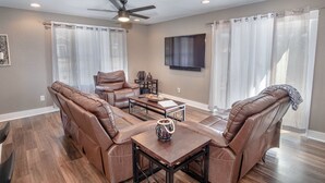 A living room with a brown leather sofa set, a coffee table, and a ceiling fan. - Lovely 3 BR Home Only 9 Minutes From Downtown (San Antonio)