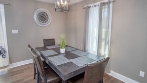 A dining room with a rectangular table, six chairs, a potted plant, a clock, and a chandelier. - Lovely 3 BR Home Only 9 Minutes From Downtown (San Antonio)