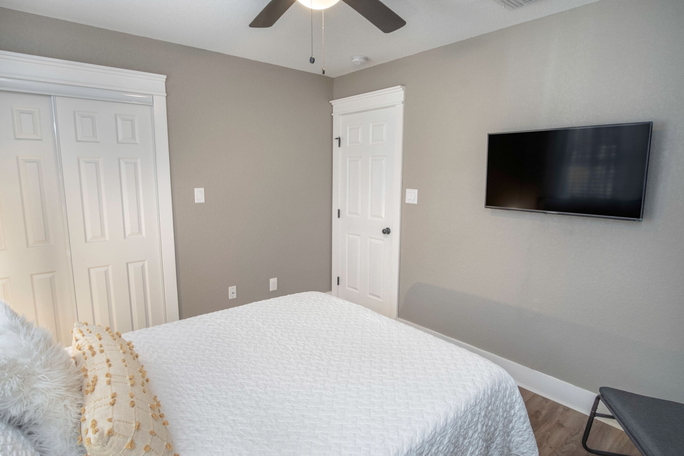 A bedroom with a bed, a ceiling fan, a TV, and two white doors.
