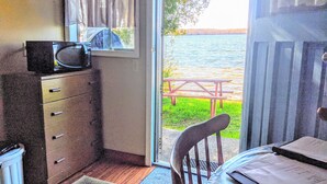 A room with a wooden dresser, a microwave, a window with checkered curtains, a view of a lake, and a picnic table outside. - Lakeview Scenic Cabin sleep 4 (Mar)