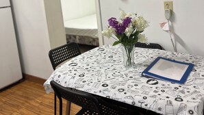 A dining area with a table covered by a tablecloth with food and kitchen utensil prints, two black chairs, a vase with flowers, and a framed quote on the wall. - Lakeview Scenic Cabin sleep 4 (Mar)