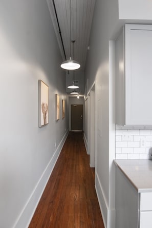 Stylish hallway leads to a modern kitchen with white cabinetry and a tiled backsplash.