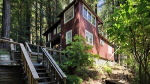 Eine zweistöckige Holzhütte mit einer Treppe, die zum Eingang führt, umgeben von dichtem Wald.