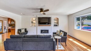 Ein geräumiges Wohnzimmer mit einem grauen Ecksofa, einem kleinen runden Tisch und einem Deckenventilator.
