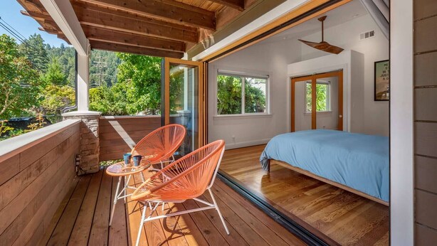 Ein Schlafzimmer mit Bett, Holzdielen und großen Fenstern.
