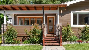 Ein modernes Haus mit einer Holzveranda, Steinstufen und einem gepflegten Garten.