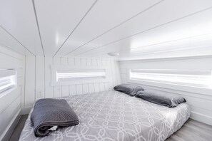 Un dormitorio con una cama, dos almohadas, una colcha y una ventana con persianas.