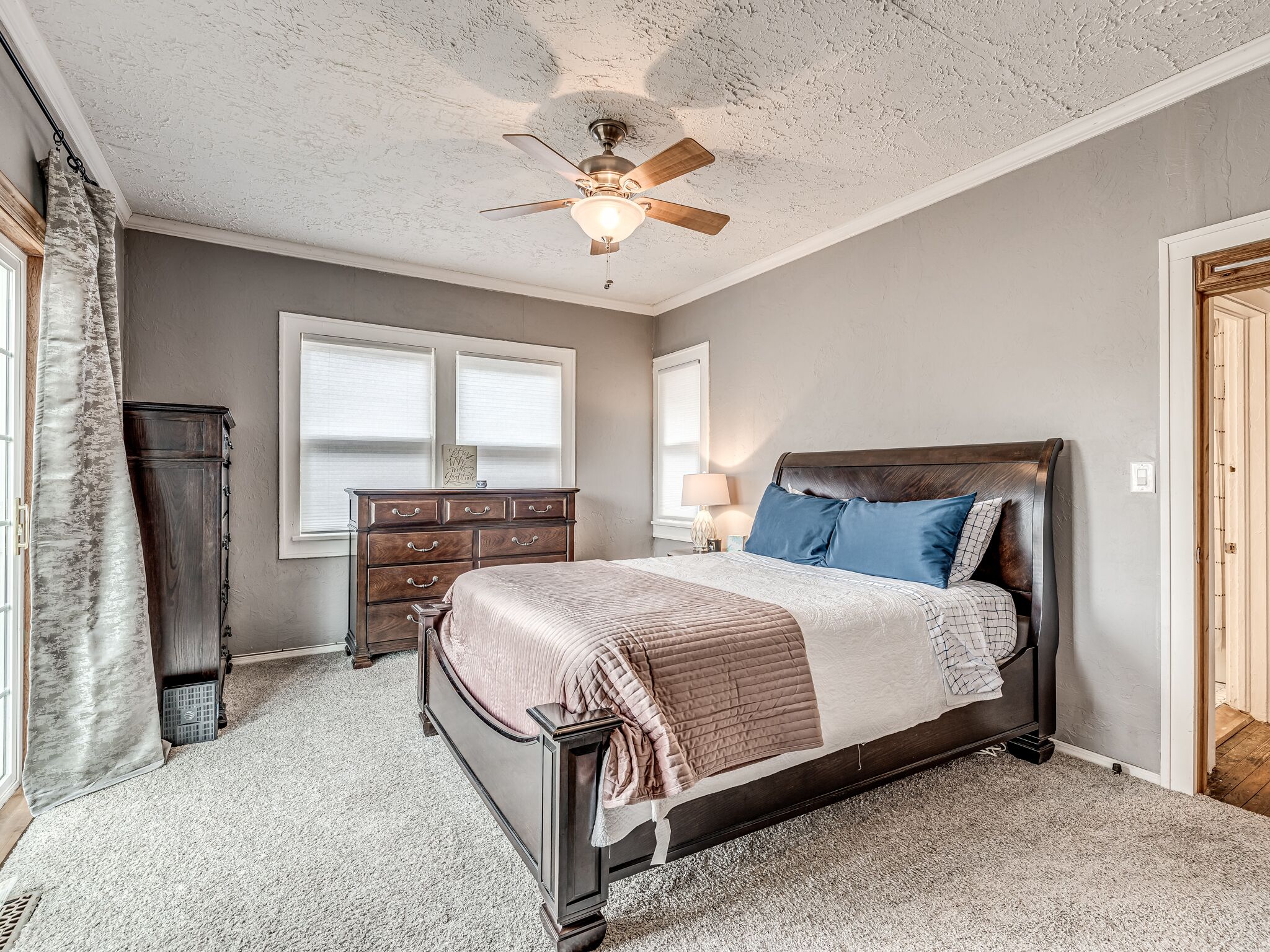 A bedroom with a bed, a dresser, a ceiling fan, and a window.