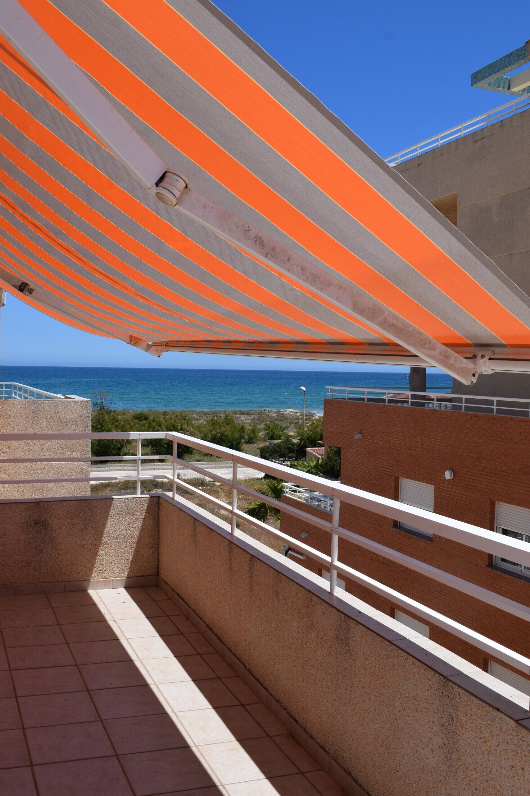 A balcony with a view of the sea, a tiled floor, and a striped awning.