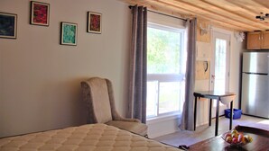 Een kamer met een bed, een stoel, een klein tafeltje, een schaal fruit en een kitchenette met een koelkast.