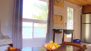 Een kamer met een houten tafel, een schaal fruit, uitzicht op het water en een keukenhoek.