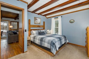 Een slaapkamer met een bed, een nachtkastje, een raam en een deur die leidt naar een andere kamer.