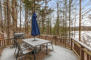 Een terras met een barbecue en tafel, omgeven door een houten balustrade en bomen.