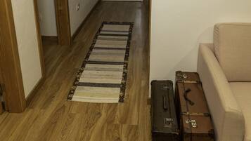 Un couloir avec un plancher en bois, un tapis à rayures, un canapé beige et deux valises.