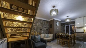 Un salon chaleureux avec un mur en pierre, un escalier en bois, un canapé et une table à manger.