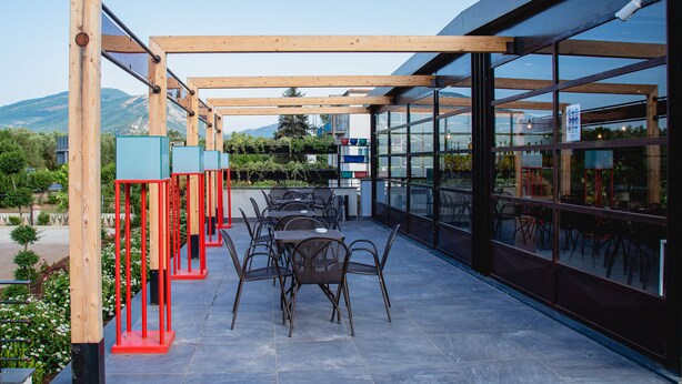 An outdoor patio with tables and chairs, wooden beams, and glass walls. - Hotel Almas Paestum (Capaccio-Paestum)