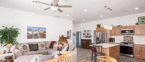 A modern living room with a sofa, a dining table, and a kitchen area with wooden cabinets and appliances.