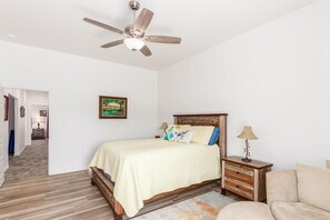Quarto com cama, mesa de cabeceira, luminária, ventilador de teto e um quadro na parede.