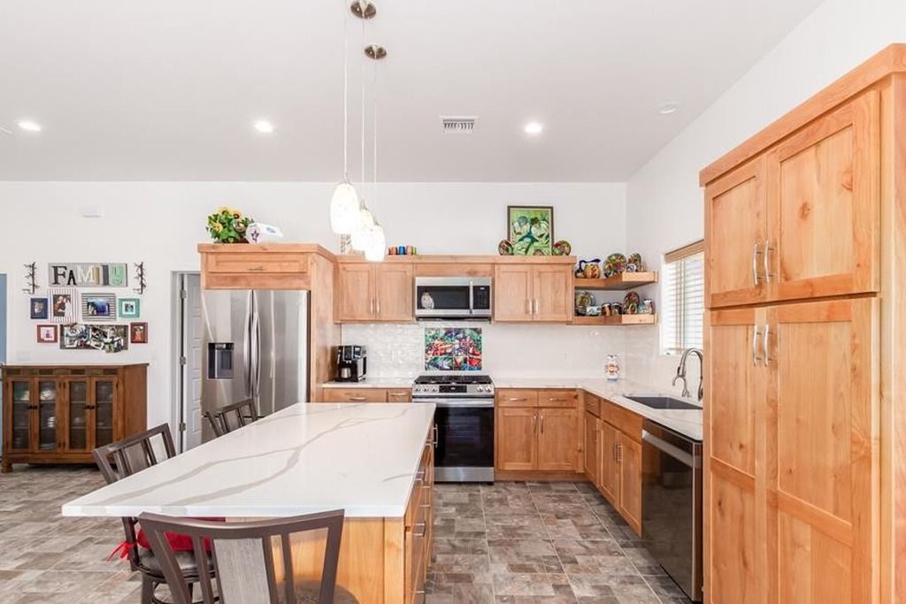 A modern kitchen with wooden cabinets, a central island, stainless steel appliances, and a tiled backsplash.
