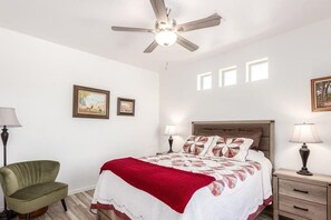 A bedroom with a bed, a ceiling fan, bedside lamps, a chair, and framed pictures on the wall.
