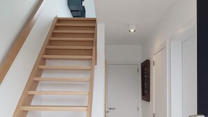 Un interior moderno con escalera de madera, paredes blancas y suelo de baldosas.