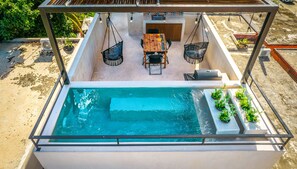 A rooftop pool with a wooden table and chairs, surrounded by potted plants and a grill. - Wayuum Suites 1: Oasis in Paradise (San Miguel de Cozumel)