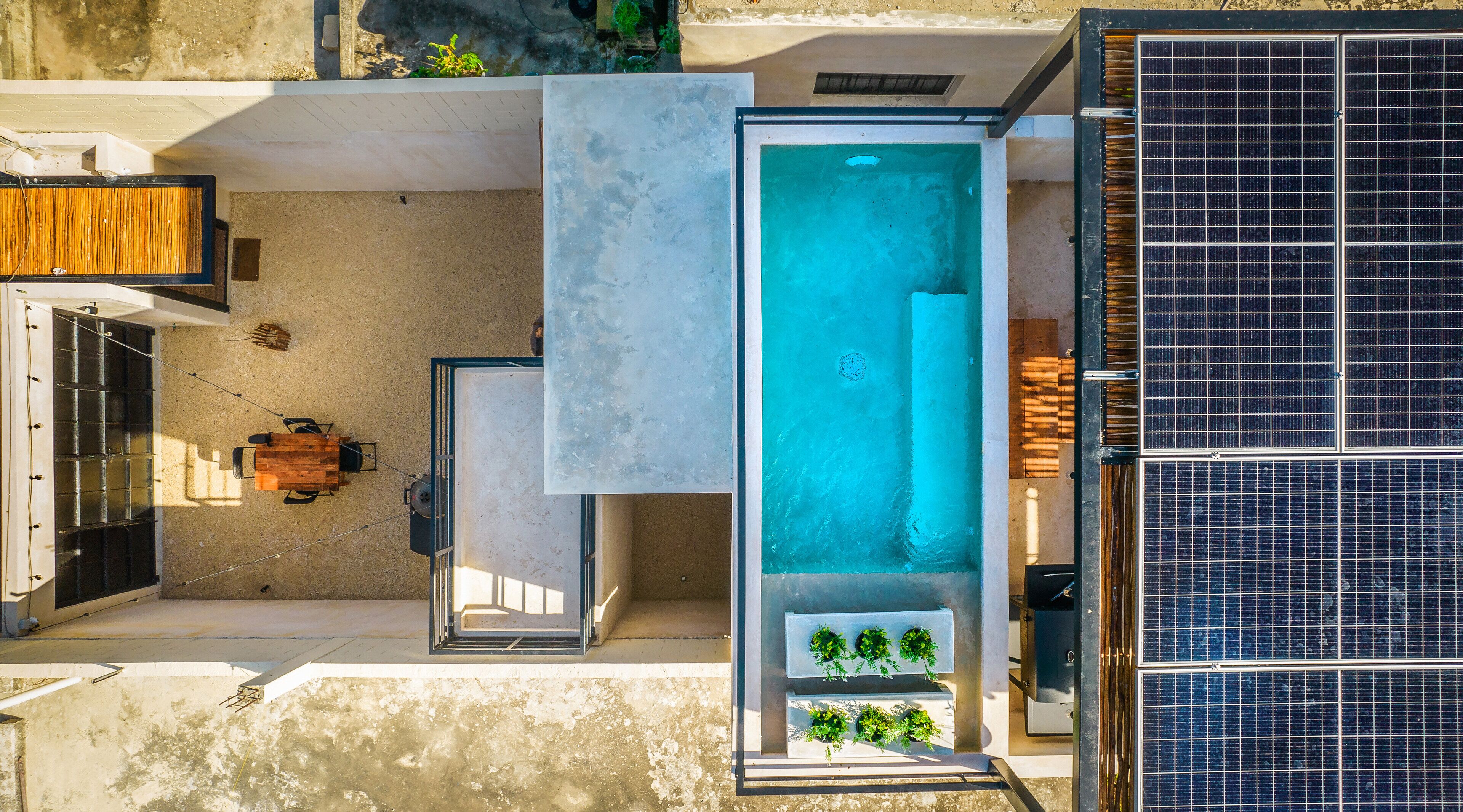 An aerial view of a modern outdoor pool area with a glass enclosure, solar panels, and a wooden deck.