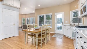 Una cocina amplia con suelo de madera, muebles blancos y un gran ventanal con vistas al exterior.