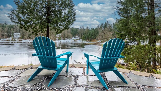 Dos sillas Adirondack azules mirando un río con árboles al fondo.