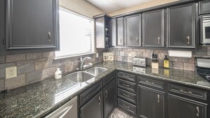 Cucina con pensili scuri, piani di lavoro in granito, un lavello doppio e forno integrato.