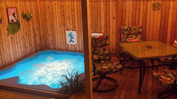 Un terrazzo in legno con una vasca idromassaggio, un tavolo e sedie.