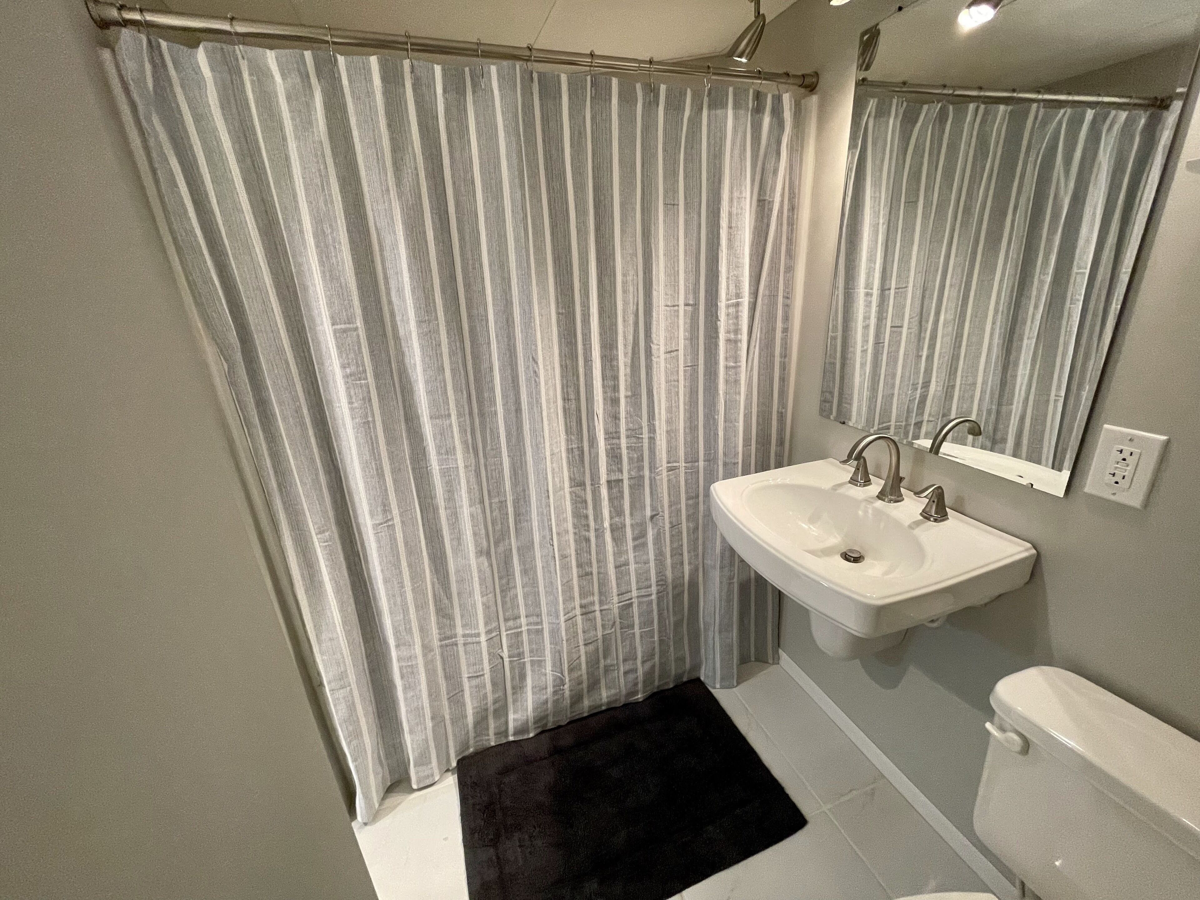 Une salle de bain avec un rideau de douche, un lavabo, un miroir et des toilettes.