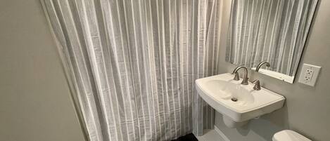 Une salle de bain avec un rideau de douche, un lavabo, un miroir et des toilettes.