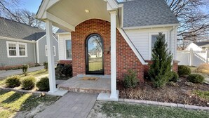 A house with a brick facade, a black front door, and a covered porch. - Cozy Double King Suite Bungalow (Great Bend)