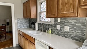 A kitchen with wooden cabinets, a white countertop, a dishwasher, and a window with stained glass. - Cozy Double King Suite Bungalow (Great Bend)