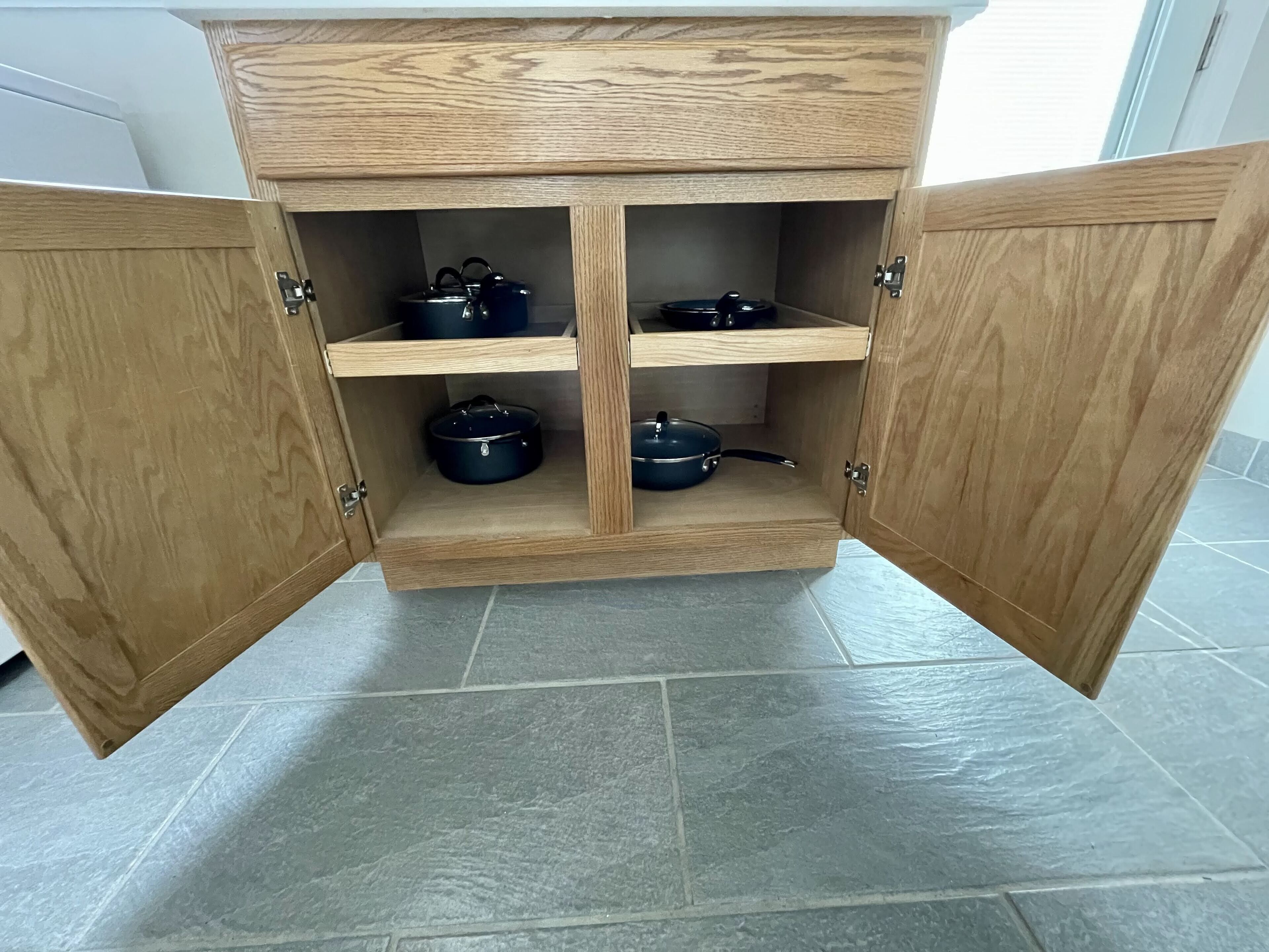 A wooden kitchen cabinet with four shelves, each holding a pot.