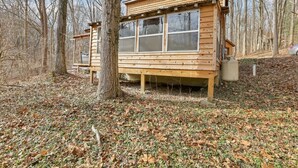 A wooden cabin with a large window, surrounded by trees and a leaf-covered ground. - The Love Shack (Hocking Hills Area) (Rockbridge)