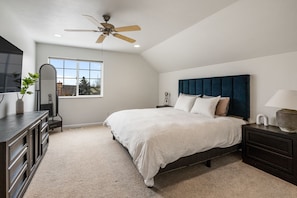Une chambre à coucher comprenant un lit, un ventilateur de plafond, une fenêtre, une commode et un miroir.