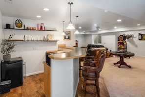 Une maison avec un îlot de cuisine, des chaises en bois, une table à manger et un jeu de fléchettes.