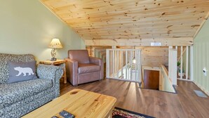 A cozy living room with a wooden ceiling, a sofa with a bear pillow, a leather armchair, and a wooden coffee table. - Cliff's Edge (Hocking Hills Area) (Amanda)