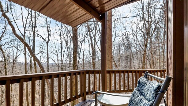A covered outdoor seating area with a wooden deck and metal chairs, overlooking a forested landscape. - Cliff's Edge (Hocking Hills Area) (Amanda)