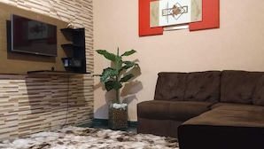 A living room with a brown sofa, a TV mounted on a wooden wall, a decorative wall piece, and a shaggy rug. - Chácara Sorriso 1 (Atibaia)