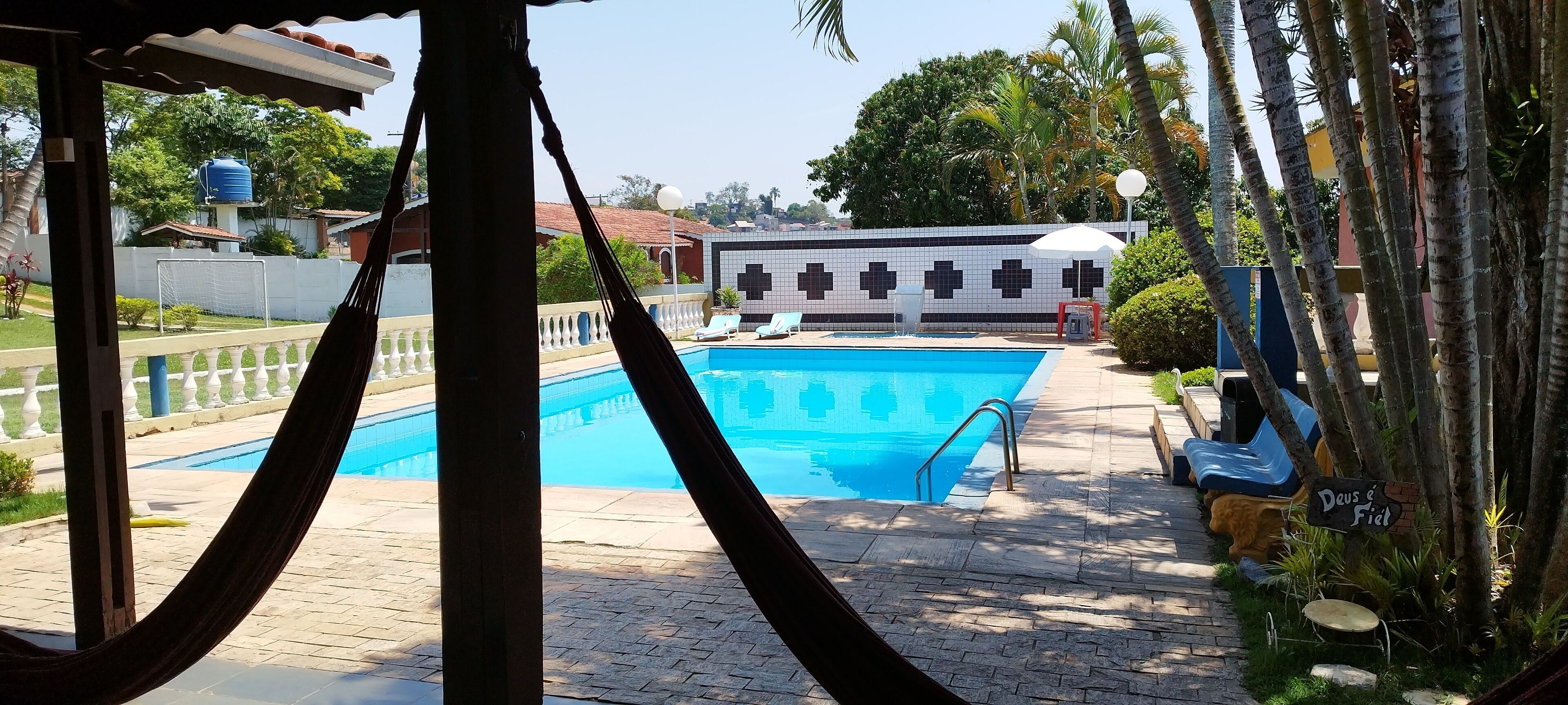 A swimming pool with a tiled deck, a white fence, and a building with a cross pattern in the background.