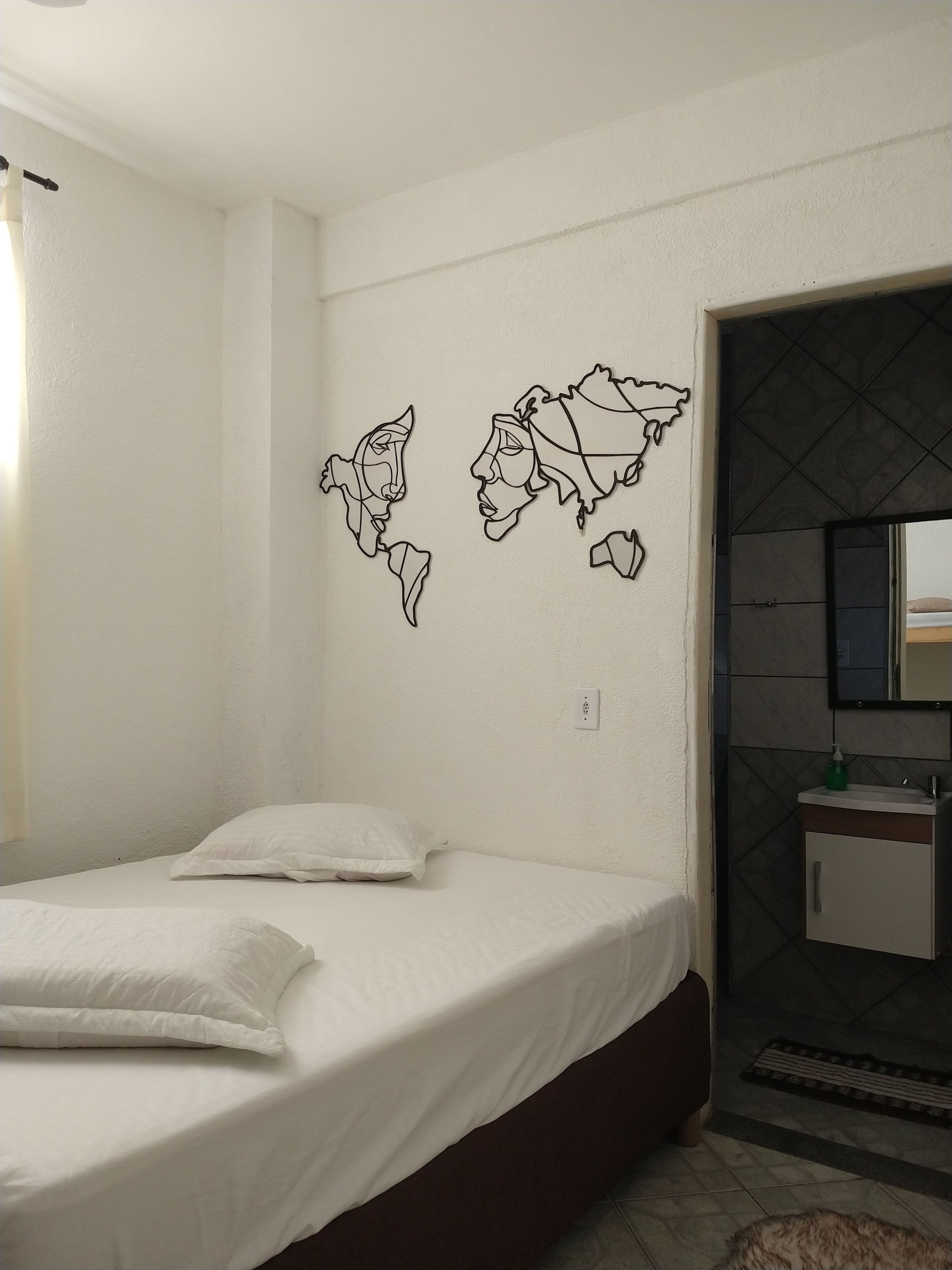 Un dormitorio con cama, paredes blancas y baño con espejo y lavabo.