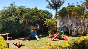 A playground with slides and climbing structures surrounded by lush greenery and a stone wall. - Chácara Sorriso 1 (Atibaia)