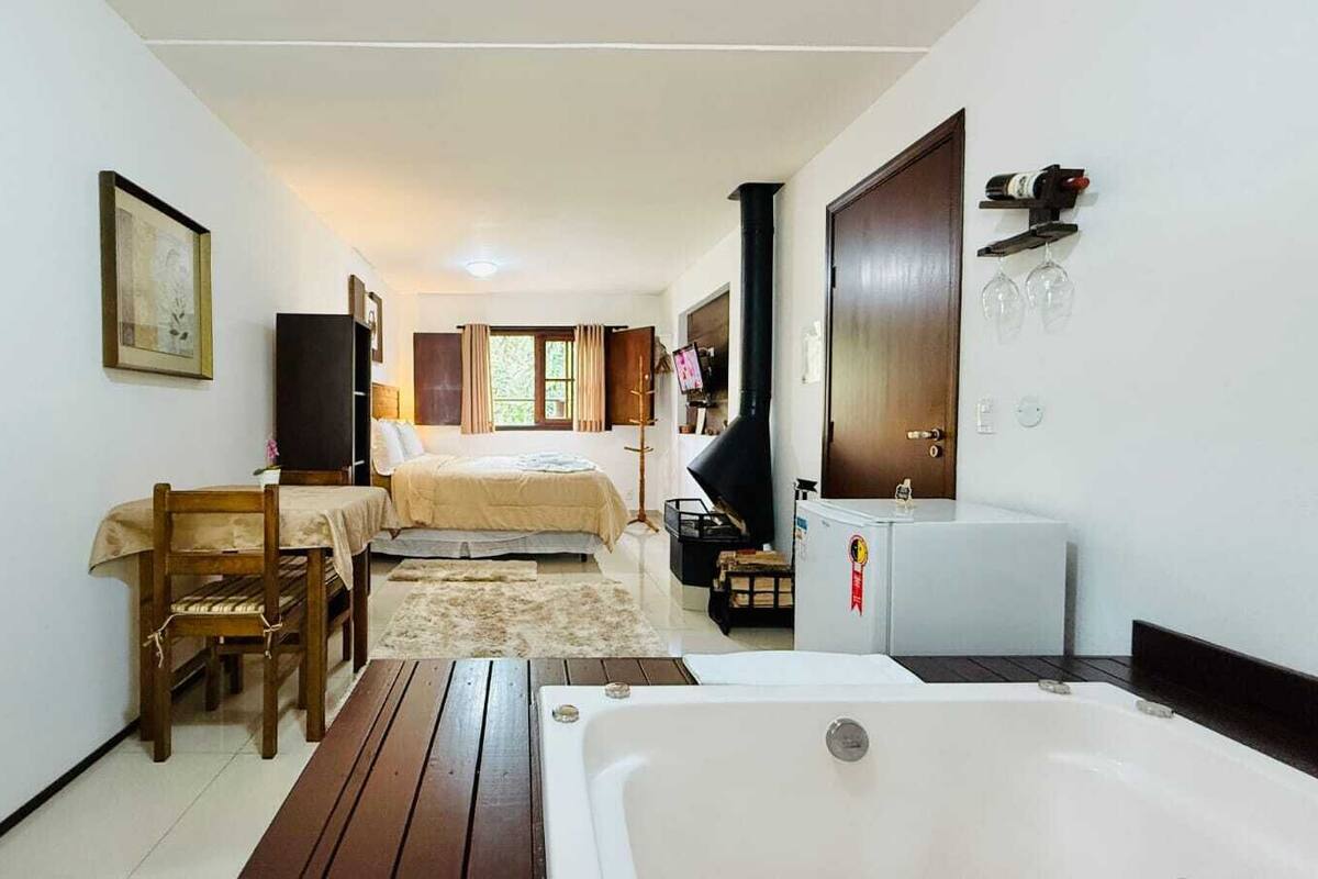 Una habitación con cama, una mesa de madera, una silla, un refrigerador pequeño y una bañera.