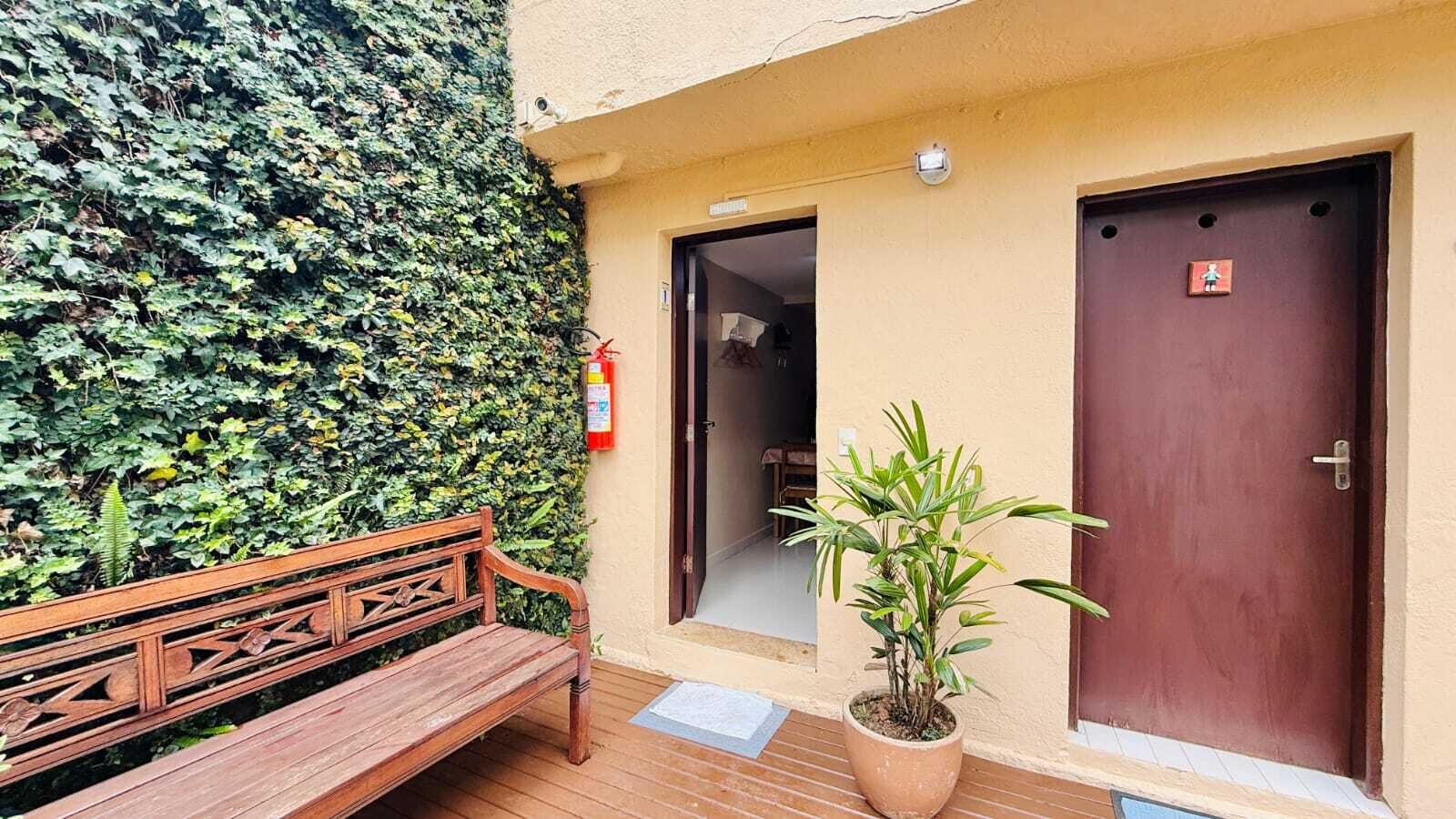 A wooden bench, a potted plant, and two doors with a fire extinguisher on the wall.