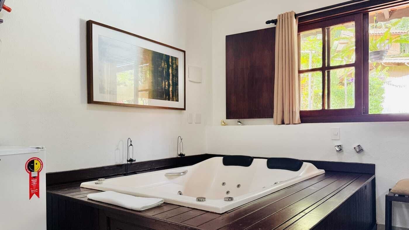 A bathroom with a large bathtub, a framed picture on the wall, and a window with curtains.