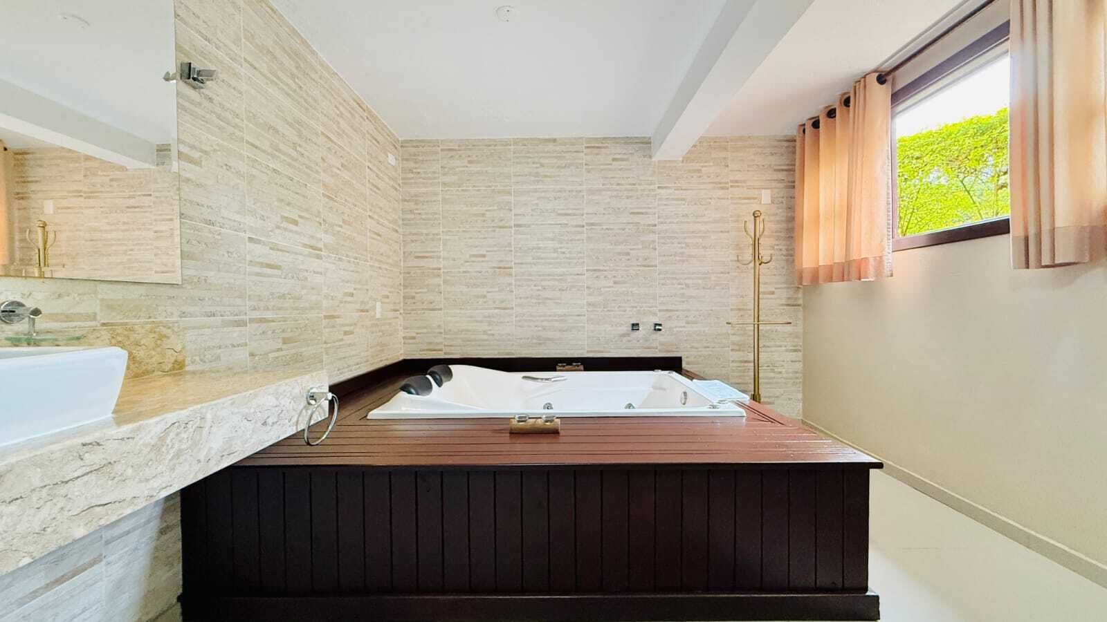 Ein modernes Badezimmer mit einer freistehenden Badewanne, einem großen Spiegel und einem Fenster mit Vorhängen.