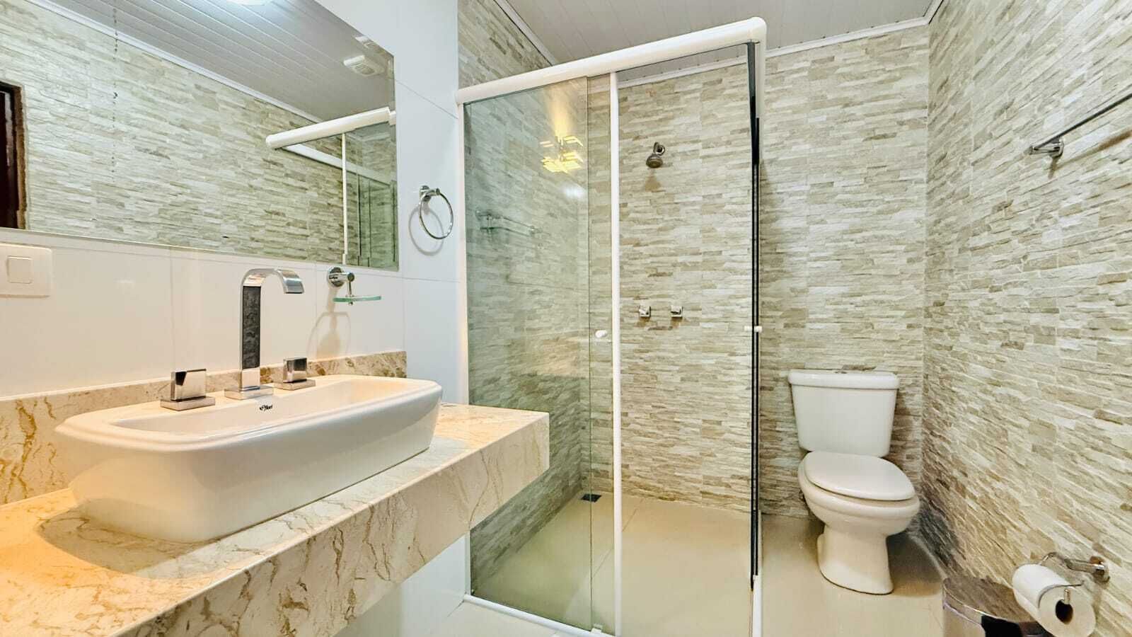 A modern bathroom with a glass-enclosed shower, a white sink with a marble countertop, and a toilet.